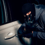 Muž v kukle sa pokúša vlámať do auta – ilustrácia krádeže vozidla.