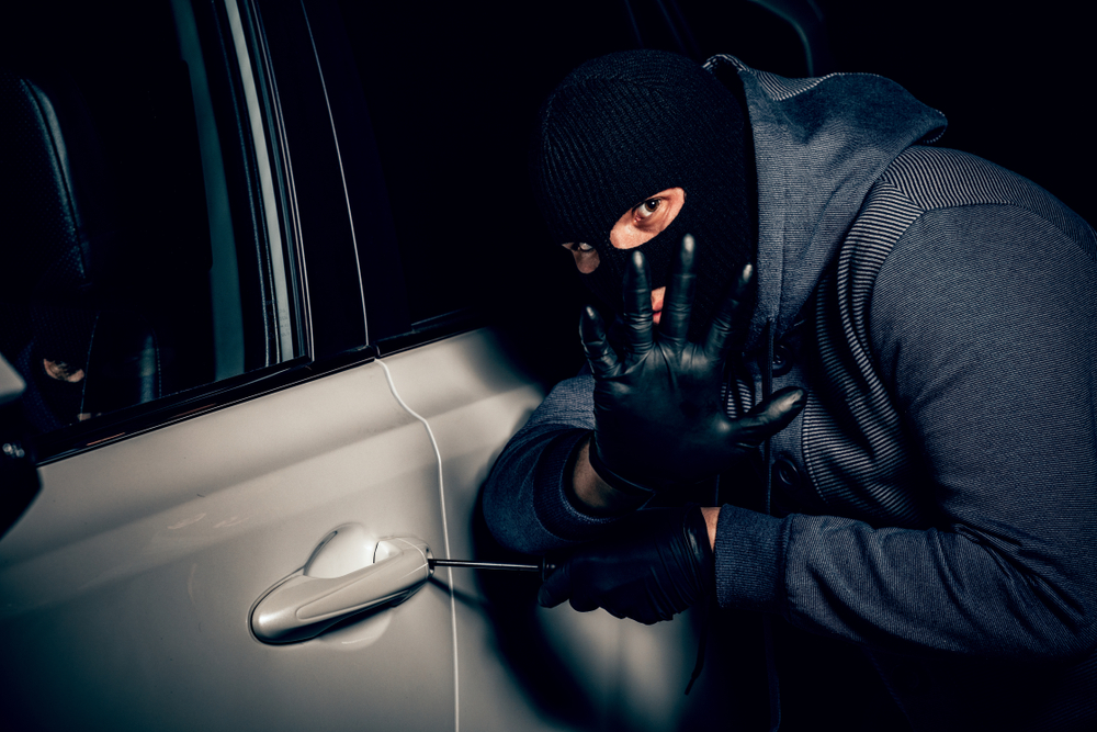 Muž v kukle sa pokúša vlámať do auta – ilustrácia krádeže vozidla.