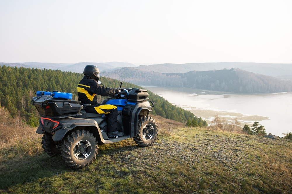 Štvorkolka zaparkovaná pri horskej chate, s pohľadom na les a kopce v pozadí.