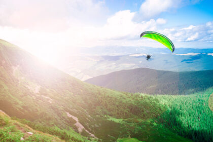 Paraglajdista na krídle padáka letiaci vysoko nad kopcami počas slnečného jarného dňa.